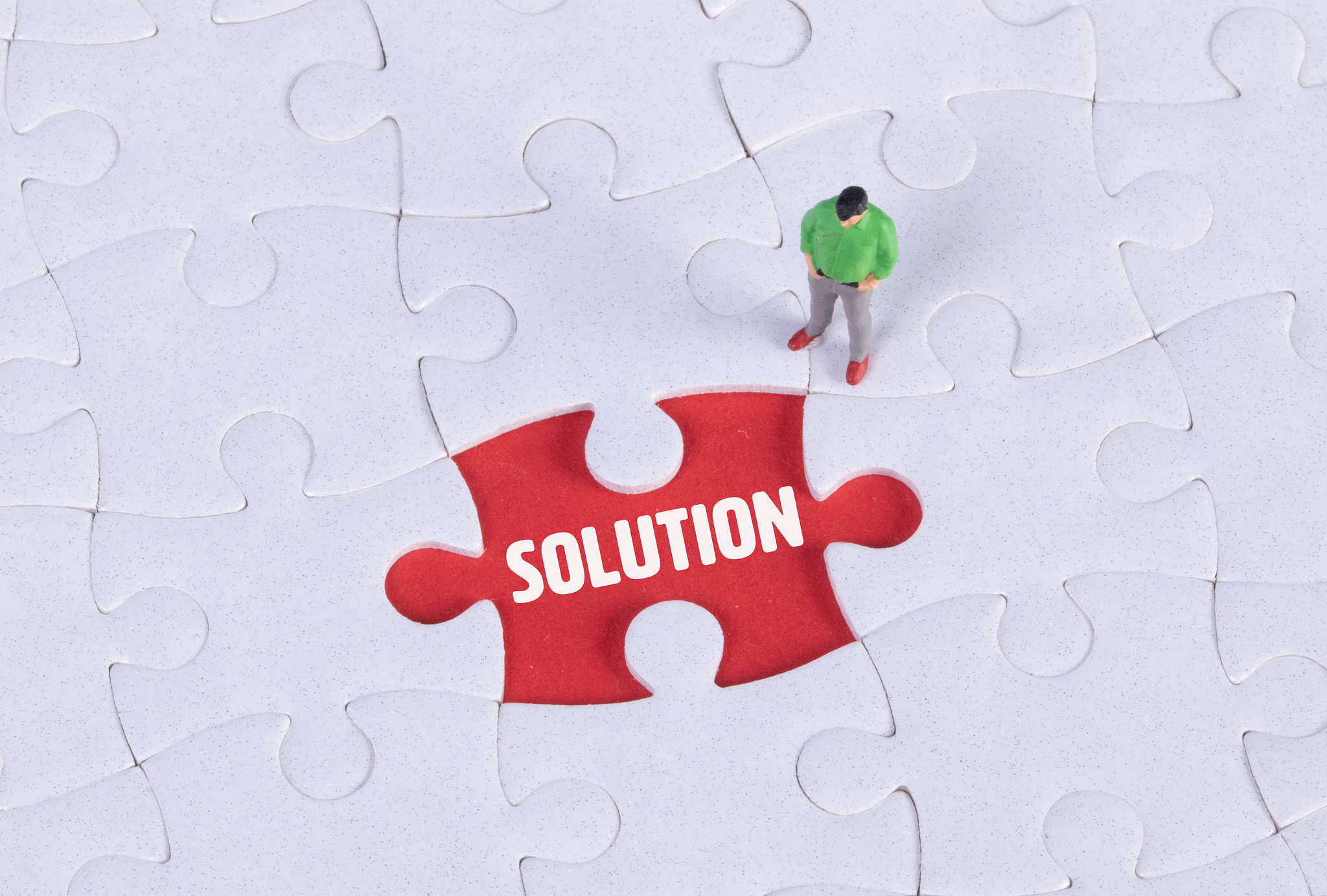 A man staring down at a puzzle, with a missing piece which reads "solution"